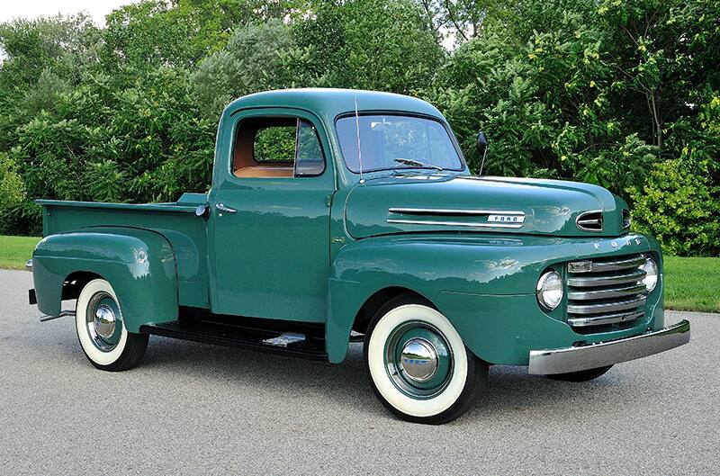 Green classic Ford F150 parked on the road in front of greenery