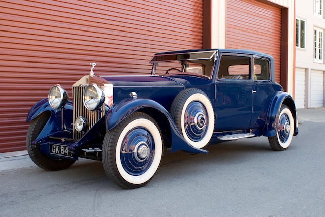 Blue Rolls-Royce Phantom II parked in from of a red garage on a sunny day