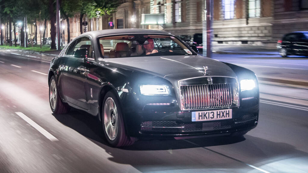 Rolls-Royce Wraith cruising down the street at night in a busy town