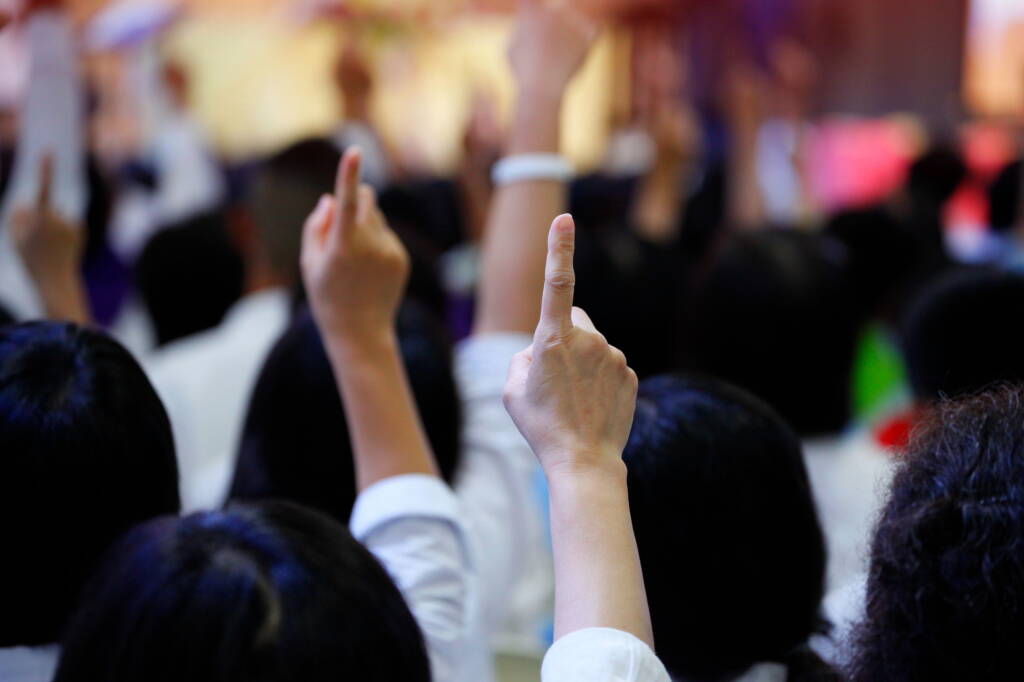 Audience raising index finger to bid at a car auction