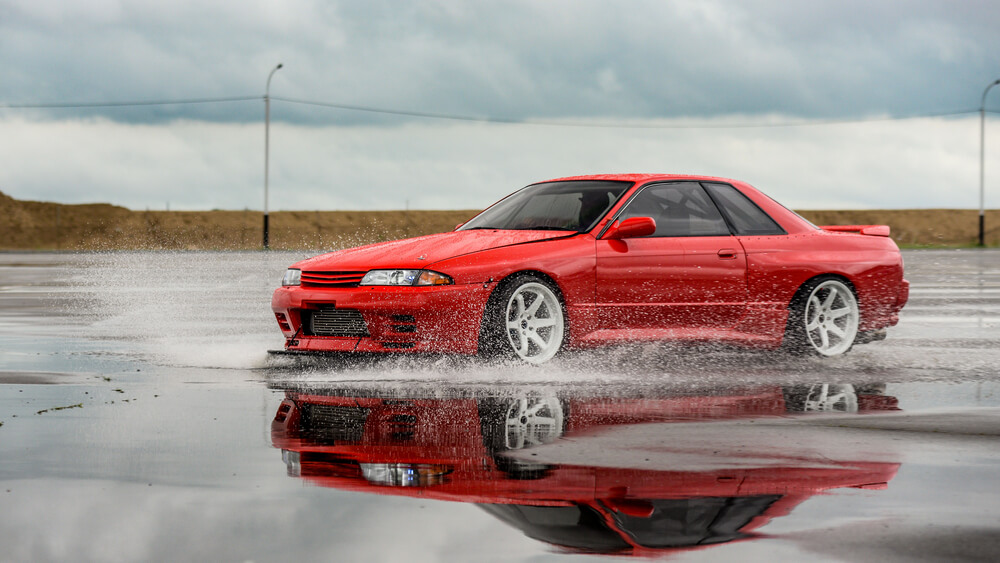 Red Nissan Skyline drifting in water puddle on the road