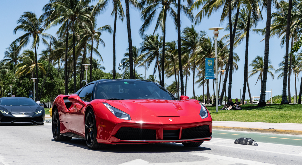 Red ferrari driving on the coast passing palm trees in Miami