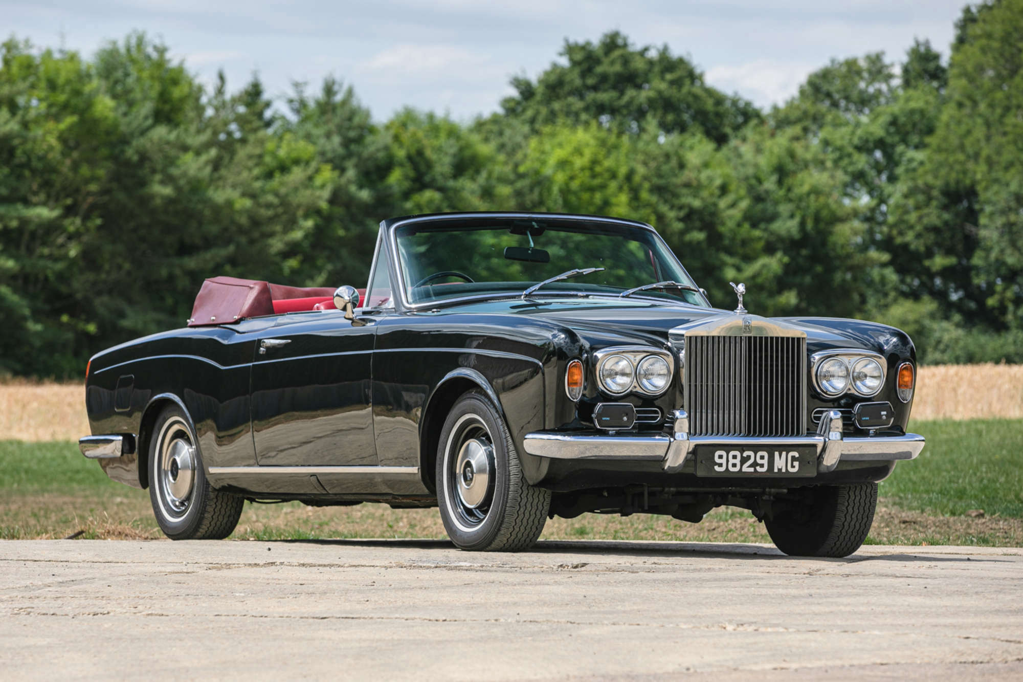 Black and red interior Rolls-Royce Corniche parked on a dirt road near grass